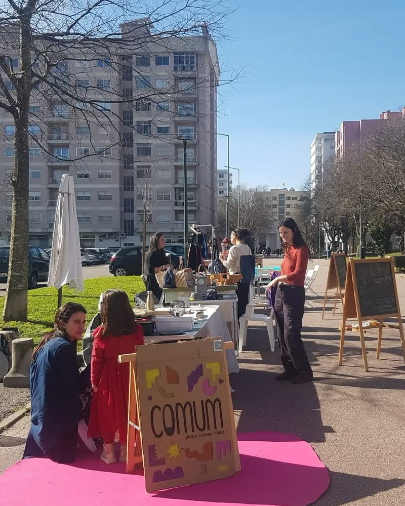 Mercado Comum realizado na Alameda Eça de Queirós com bancas e participantes a promover a economia circular e a reutilização de produtos.